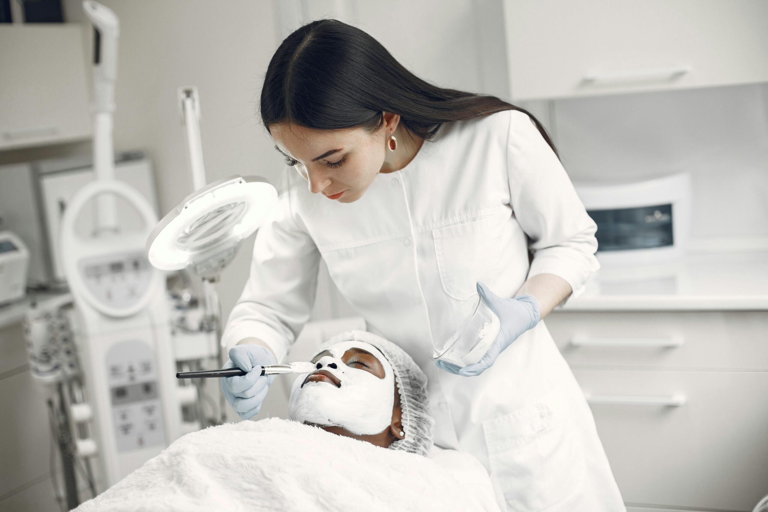 A beautician applies a face mask to a client in a beauty clinic, focusing on skincare and relaxation.